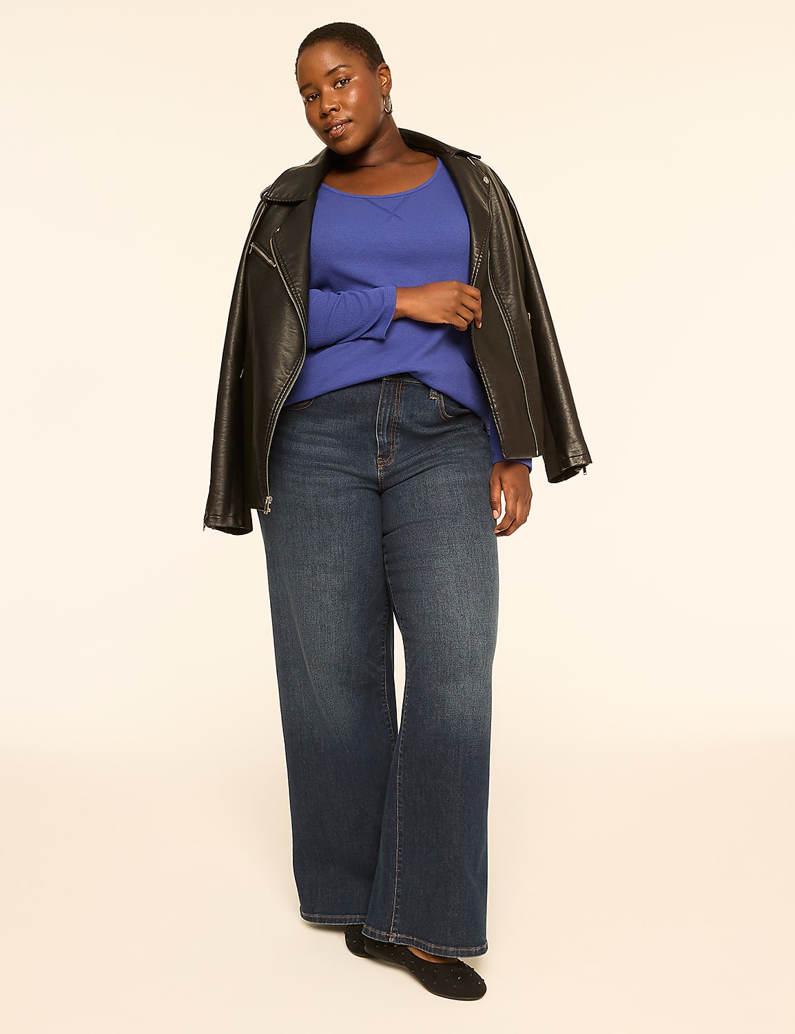A woman in a blue top, dark jeans, and a black leather jacket stands against a plain, light-colored background. Product Image 3