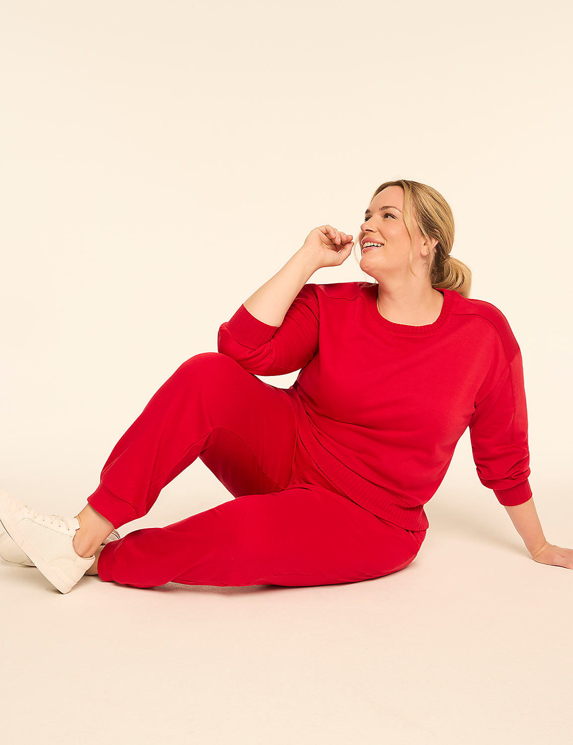 A woman in a red tracksuit sits on a plain, light-colored background, looking up and to the side with a smile. Product Image 3