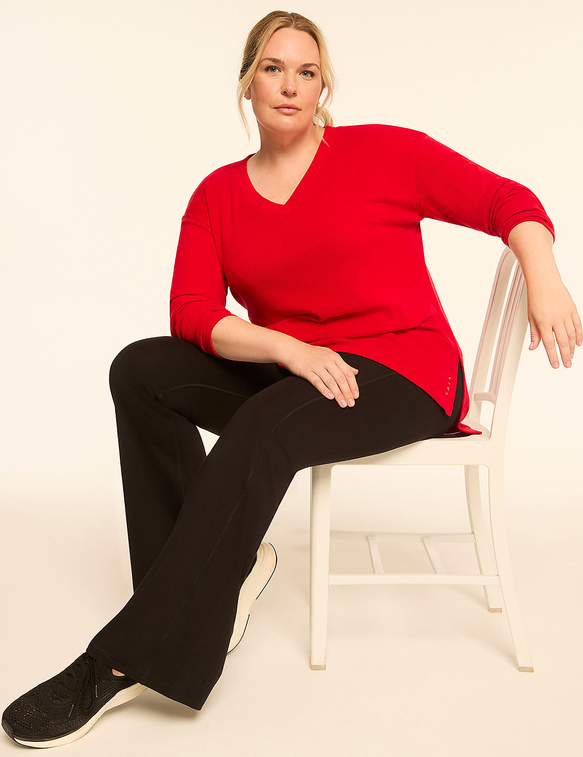 A woman in a red sweater and black pants sits on a white chair against a plain, light background. Product Image 3