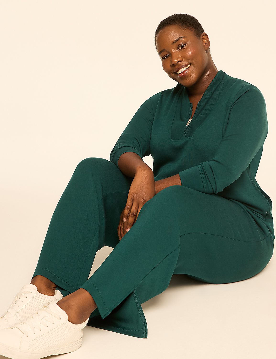 A smiling woman in a teal tracksuit and white sneakers sits on a plain, light-colored background. Product Image 3