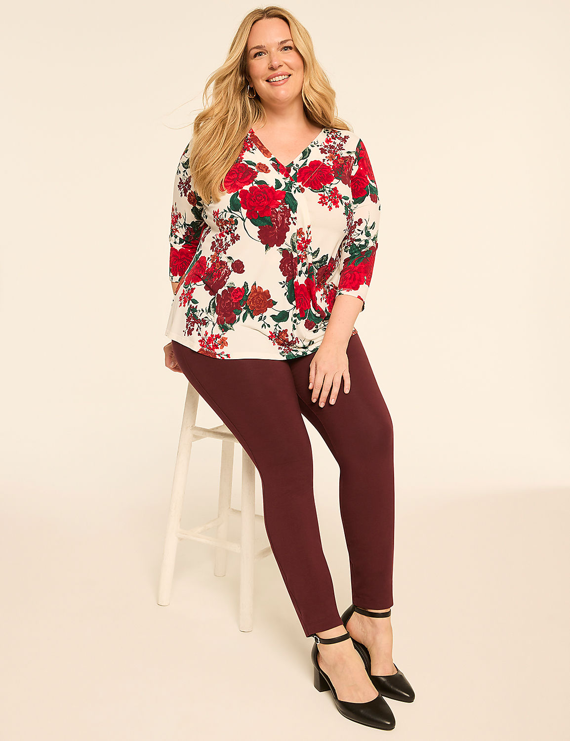A smiling woman with blonde hair sits on a white stool in the foreground, wearing a floral top and maroon leggings, against a plain, light-colored background. Product Image 3