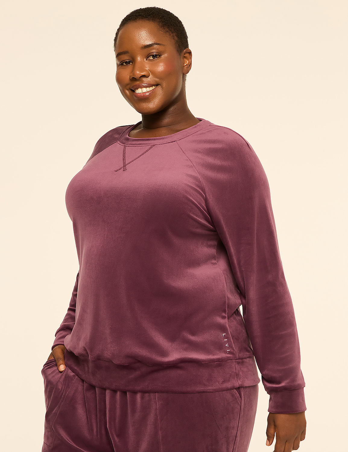 A smiling woman in a purple velvet sweatshirt and pants stands against a plain, light-colored background. Product Image 1