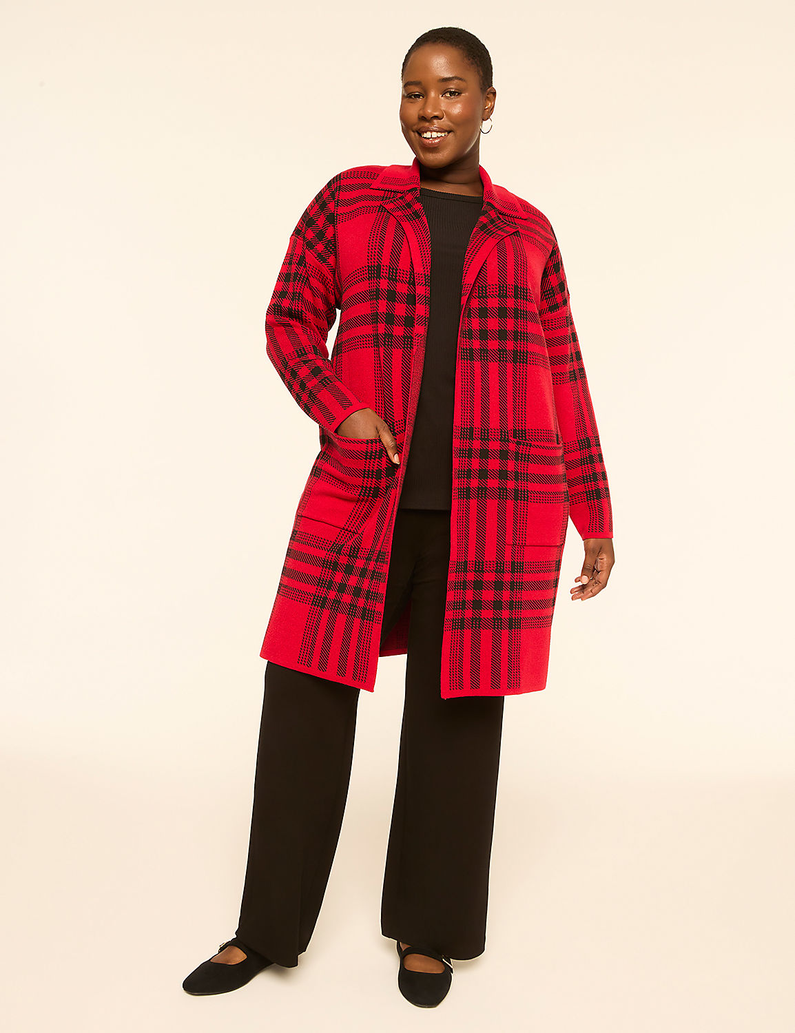 A smiling woman in a red and black plaid cardigan and black pants stands against a plain, light-colored background. Product Image 1