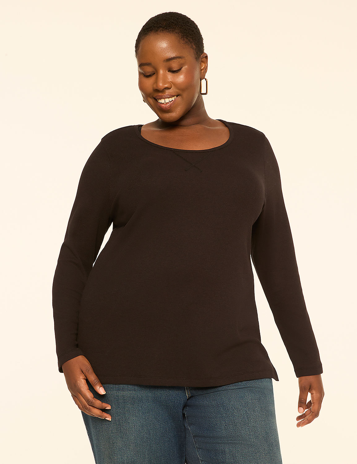 A smiling woman in a black long-sleeved shirt and blue jeans stands against a plain, light-colored background. Product Image 1
