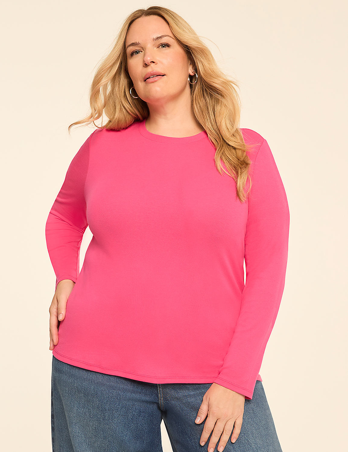 A blonde woman in a pink long-sleeved shirt and blue jeans stands against a plain, light-colored background. Product Image 1