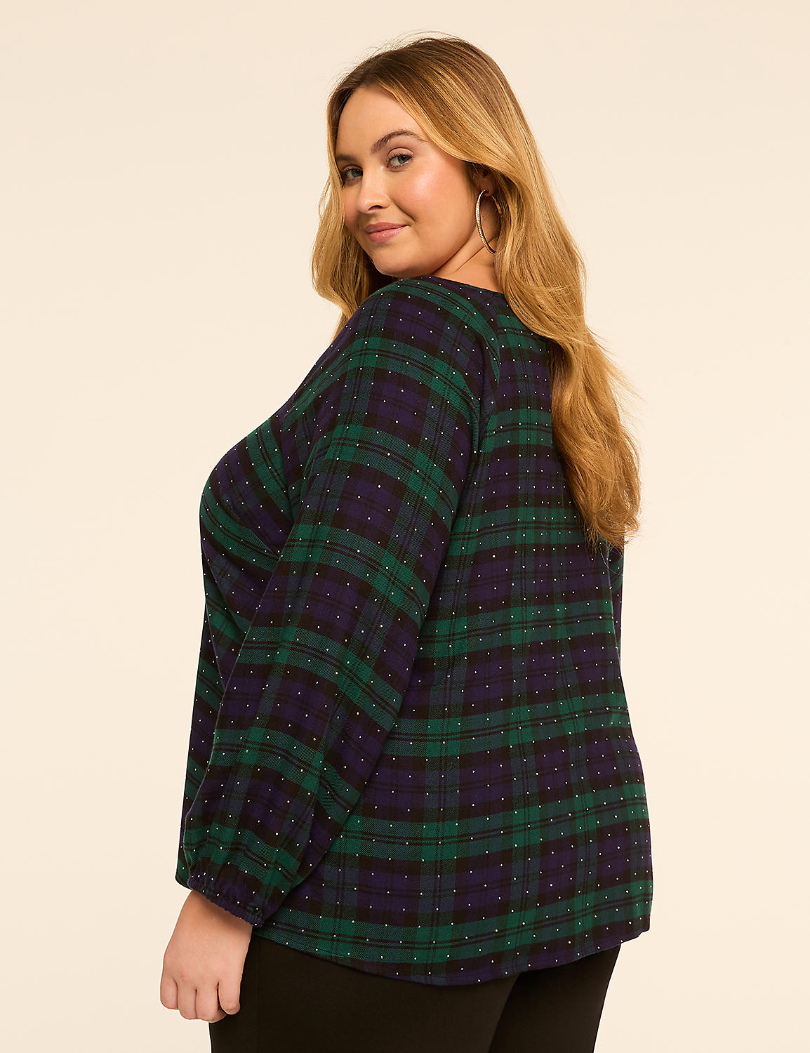 A woman in a green and navy plaid top with white polka dots poses against a plain, light brown background. Product Image 2
