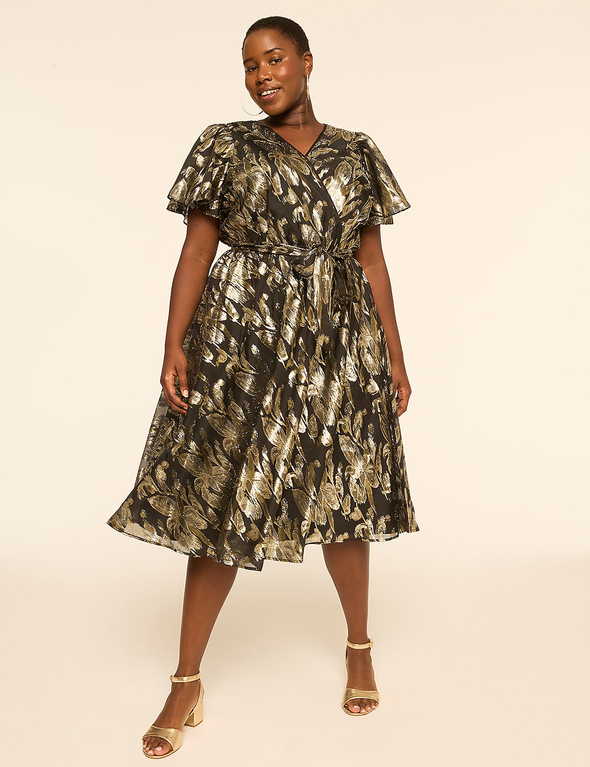 A woman in a black and gold patterned wrap dress stands against a plain, light-colored background. Product Image 1