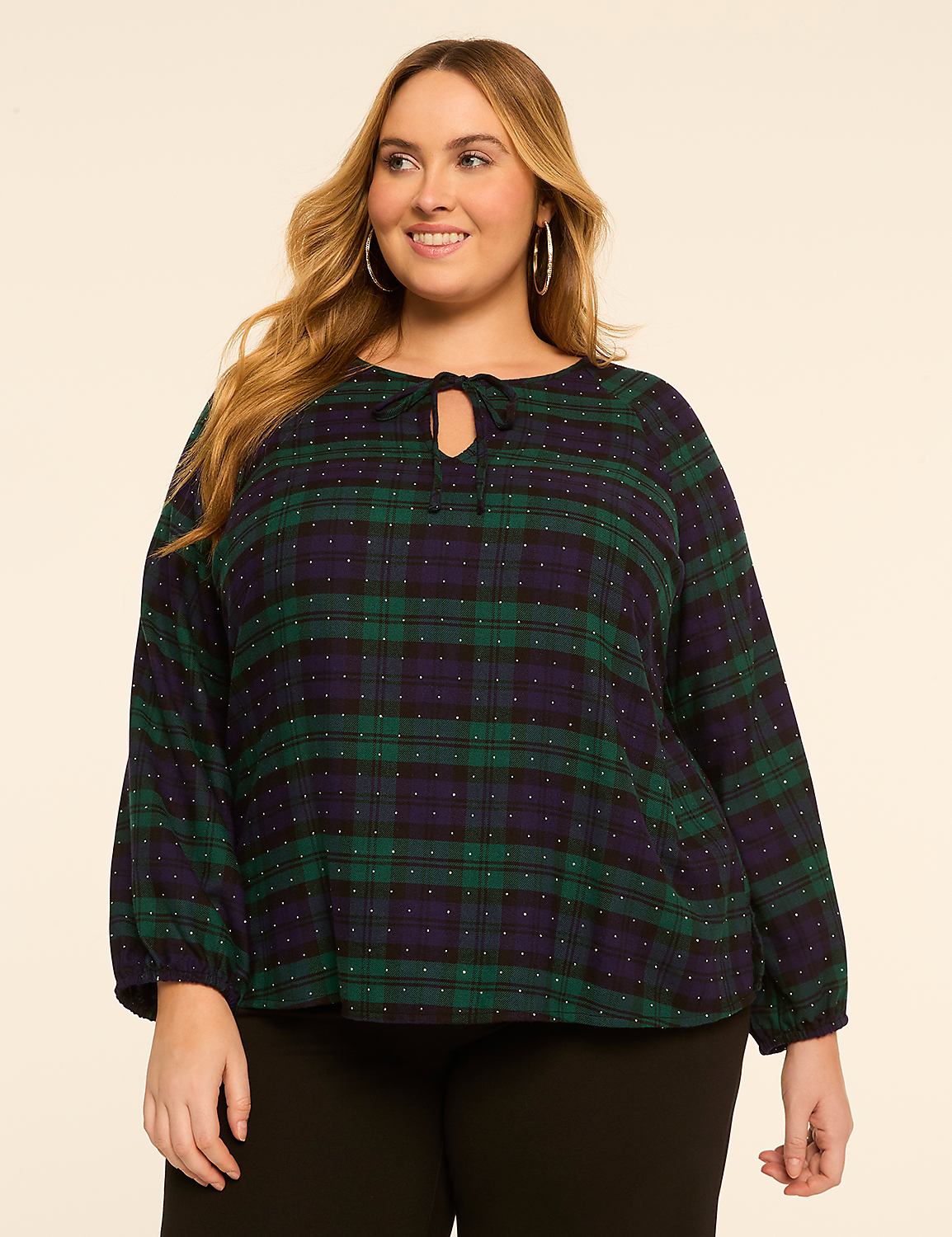 A woman with blonde hair and hoop earrings smiles at the camera, wearing a green and navy plaid blouse with a tie-neck detail, against a plain, light-colored background. Product Image 1