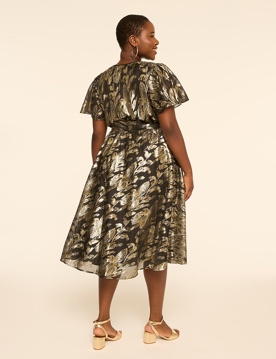 A woman in a black and gold patterned dress stands against a plain, light-colored background. Product Image 2