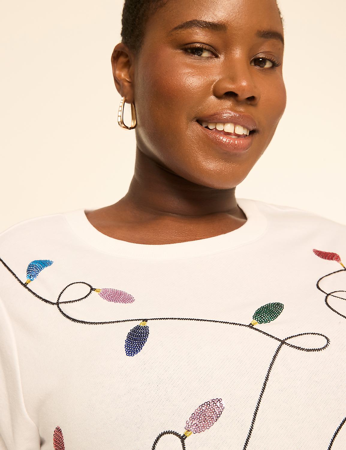 A woman smiles in the foreground, wearing a white shirt adorned with colorful sequined Christmas lights, against a plain, light-colored background. Product Image 4