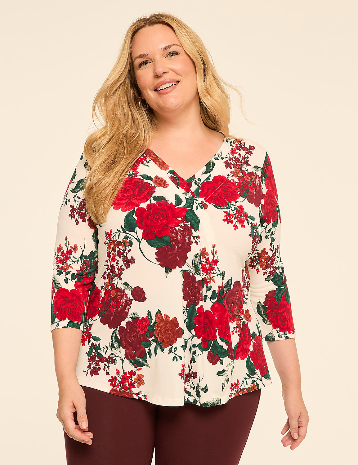 A smiling woman with blonde hair poses in a cream-colored top with a red floral print against a plain beige background. Product Image 1