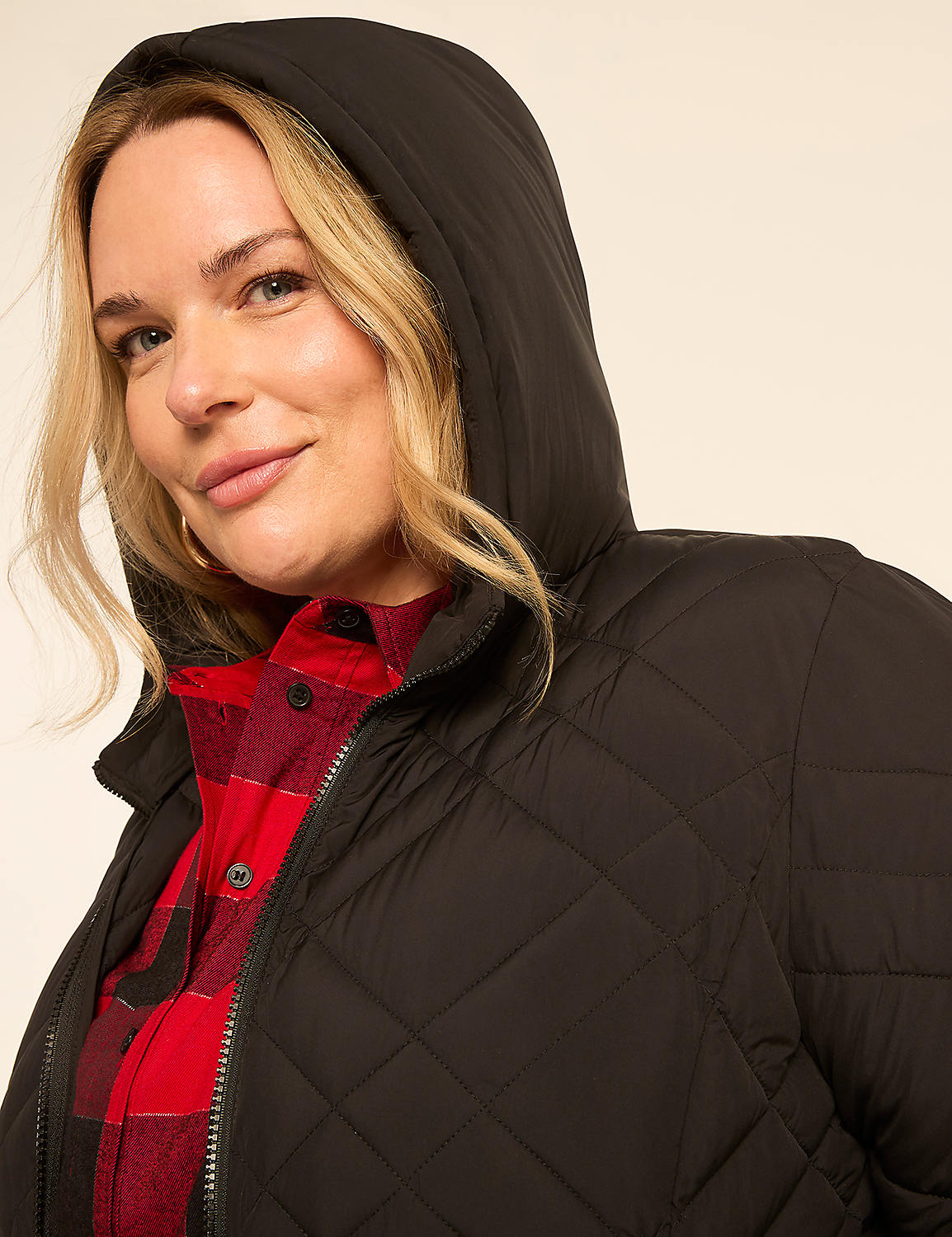 A blonde woman in a red plaid shirt and a black quilted hooded jacket smiles at the camera against a plain, light background. Product Image 3