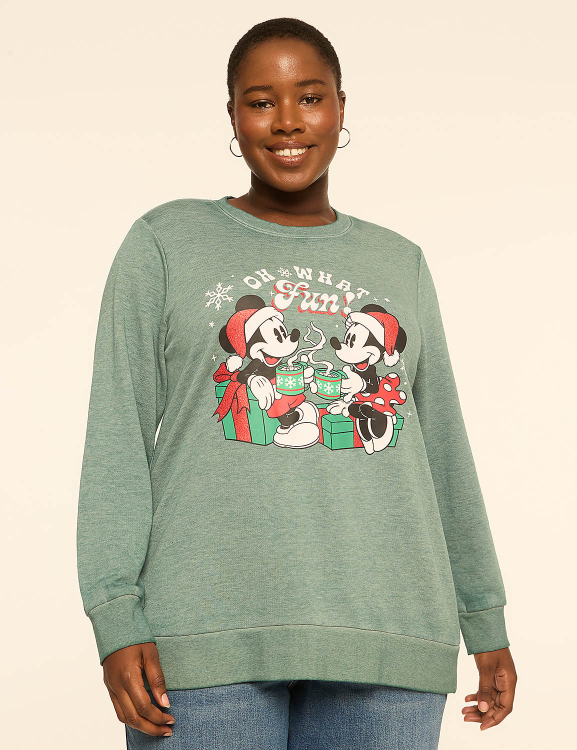 A woman in a green long-sleeved shirt with a Mickey and Minnie Mouse holiday graphic stands against a plain, light-colored background. Product Image 1