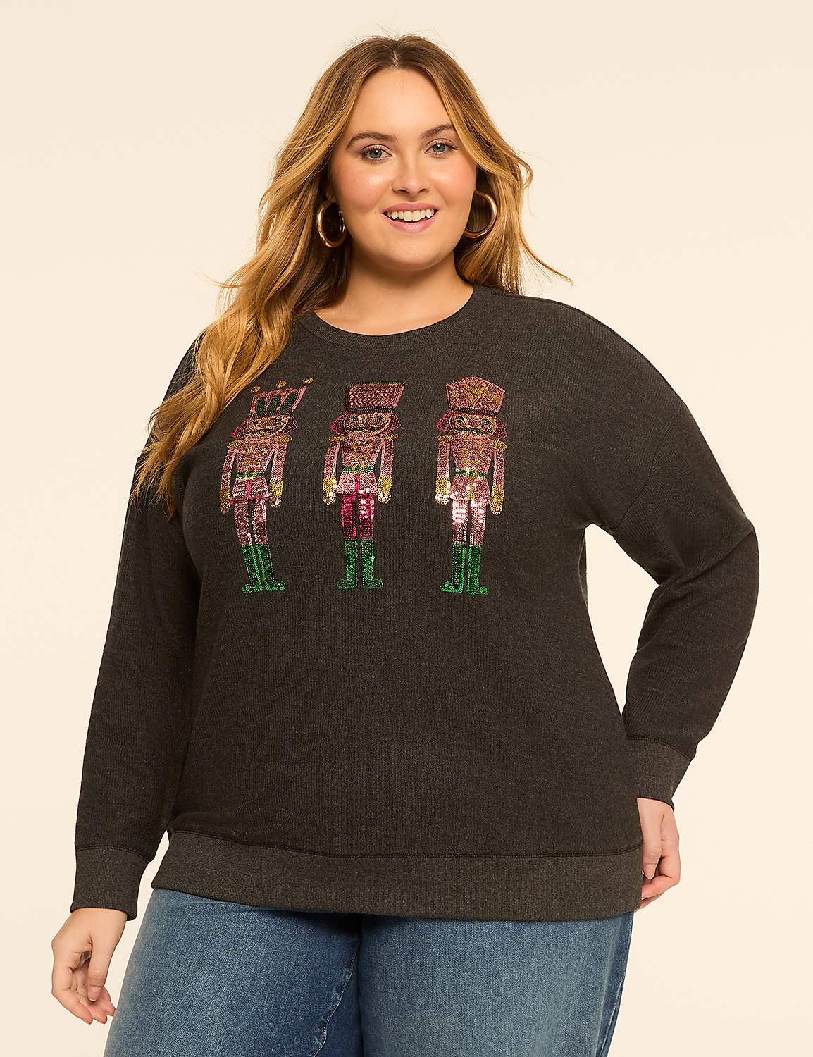 A woman in a dark grey sweatshirt with sequined nutcracker figures stands against a plain, light-colored background. Product Image 1