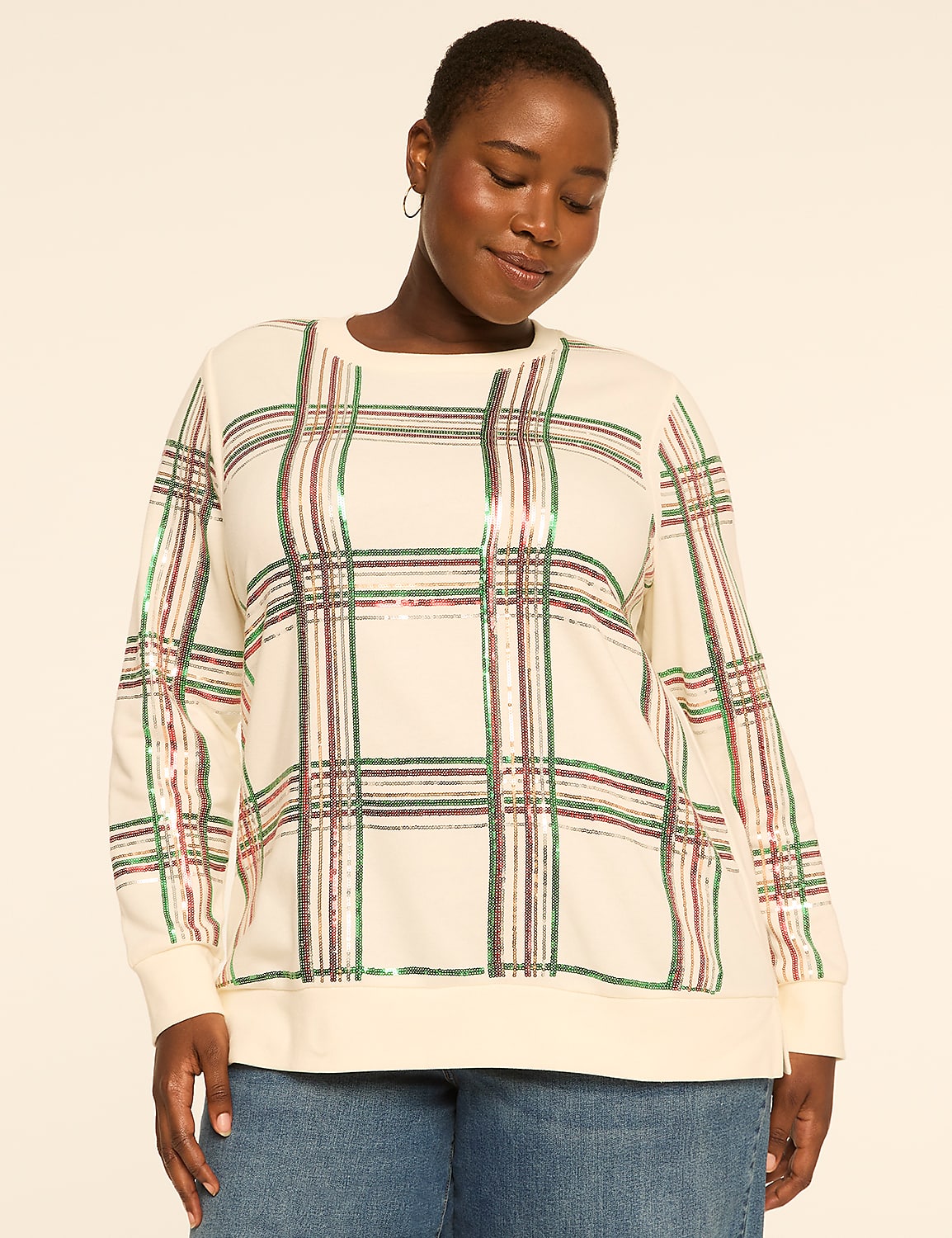 A woman in a cream-colored, plaid sweatshirt stands against a plain, light brown background. Product Image 1