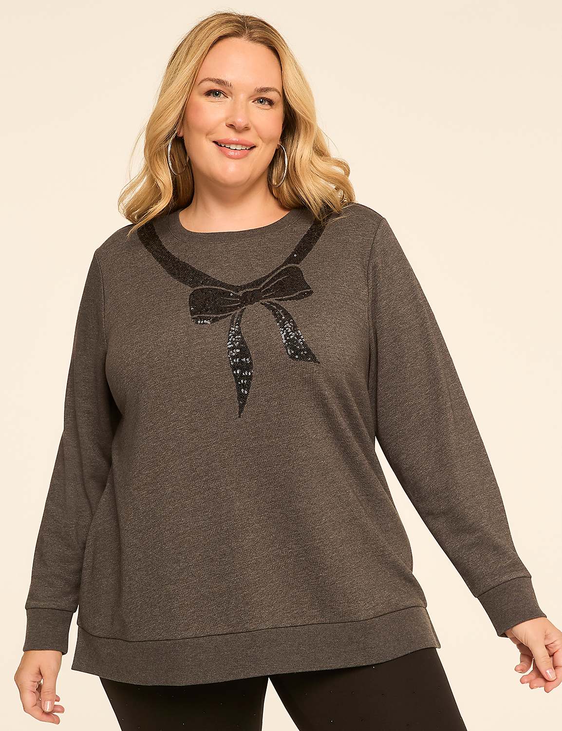 A woman in a dark grey sweatshirt with a sequined bow neckline stands against a plain, light beige background. Product Image 1