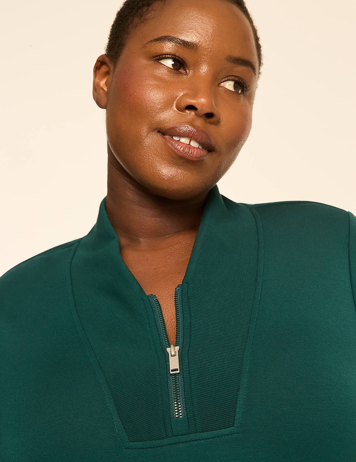 A woman with short hair smiles softly in a green quarter-zip sweatshirt against a plain, light-colored background. Product Image 4