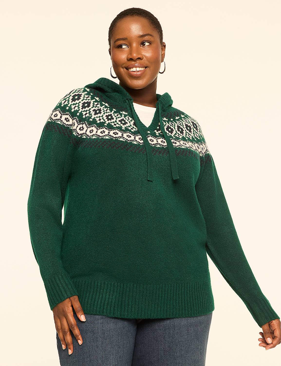 A smiling woman in a green hooded sweater with a fair isle pattern stands against a plain, light-colored background. Product Image 1
