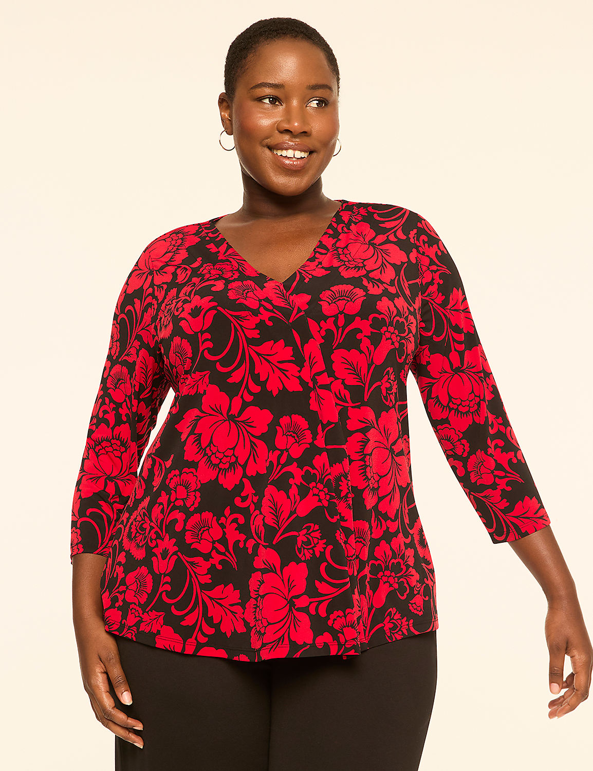 A smiling woman in a red and black floral top stands against a plain, light-colored background. Product Image 1