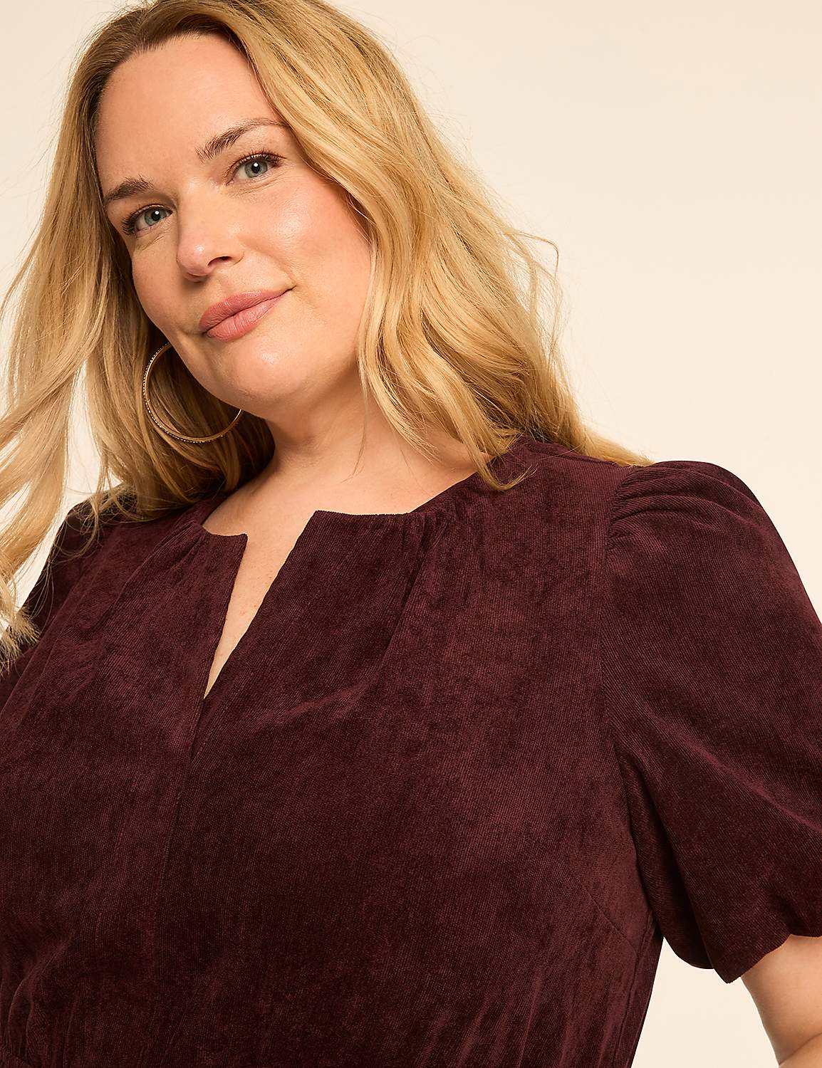 A blonde woman with hoop earrings smiles gently in a burgundy corduroy dress against a plain, light-colored background. Product Image 3