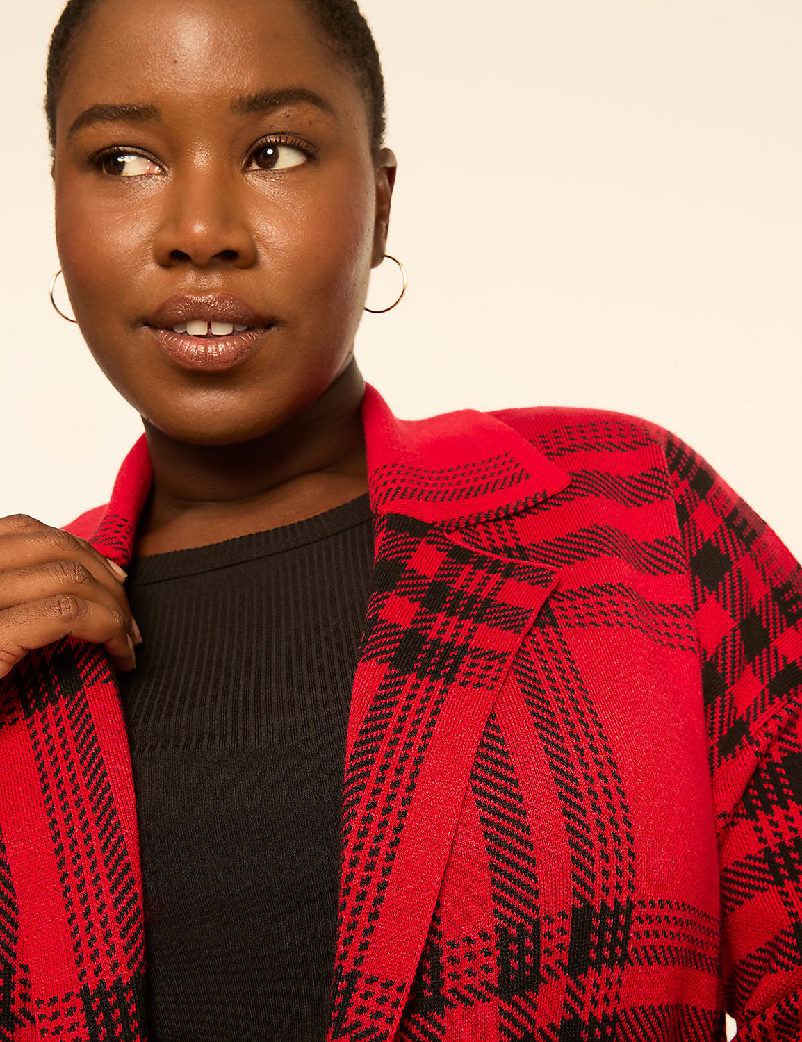 A woman with short hair and hoop earrings in the foreground wears a red and black plaid jacket over a black ribbed shirt, against a plain, light-colored background. Product Image 3