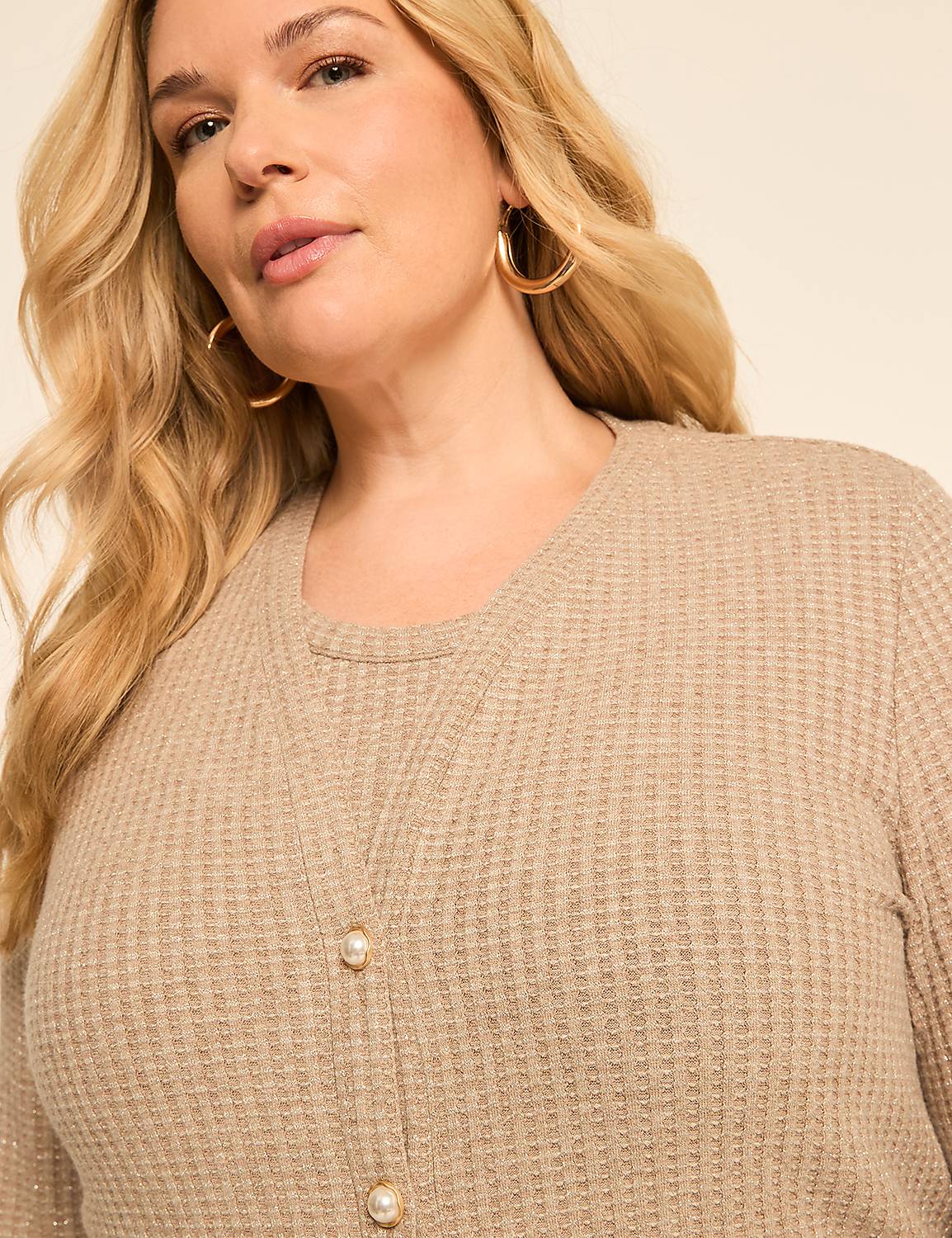 A woman with blonde hair and hoop earrings wears a beige waffle-knit top with pearl buttons, against a plain, light-colored background. Product Image 4