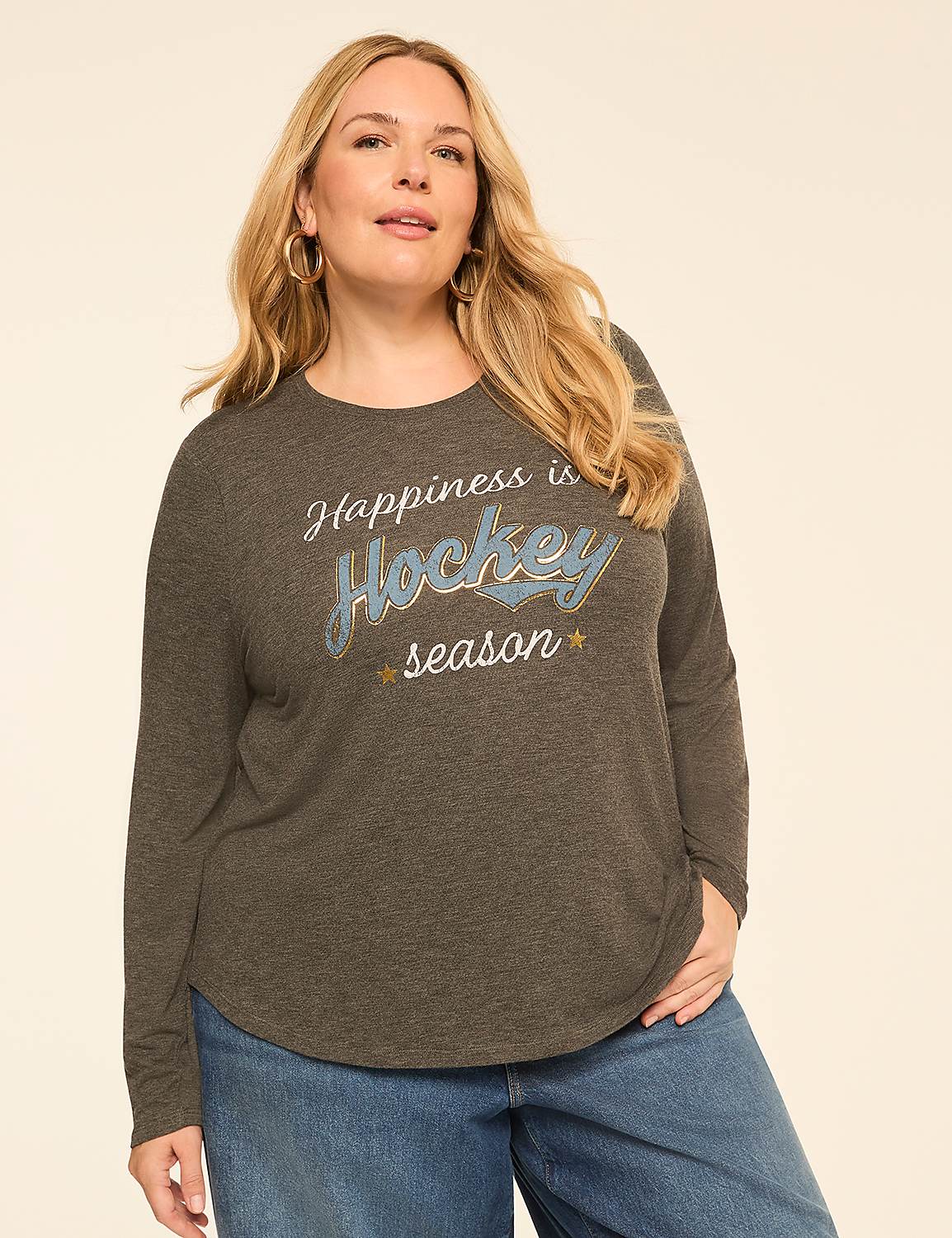 A woman in a long-sleeved shirt with "Happiness is Hockey season" printed on it stands against a plain, light-colored background. Product Image 1