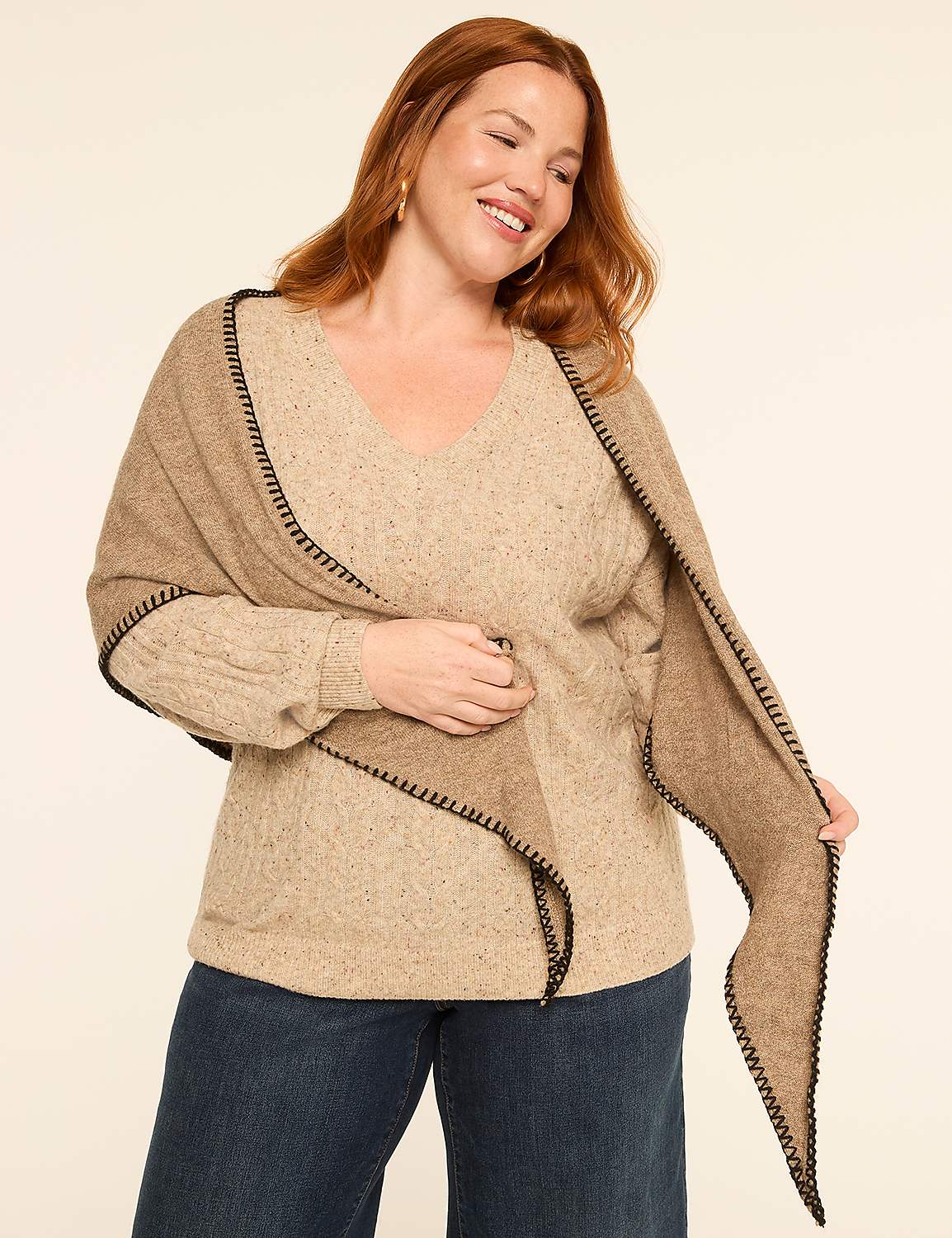 A smiling woman in a beige sweater and blue jeans poses in front of a plain, light-colored background, draped in a tan shawl with black trim. Product Image 3