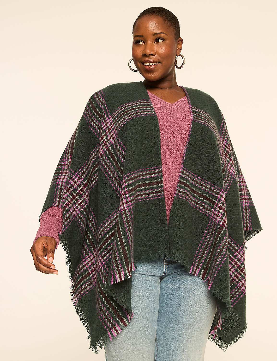 A woman in a plaid poncho and pink sweater smiles against a plain background. Product Image 1