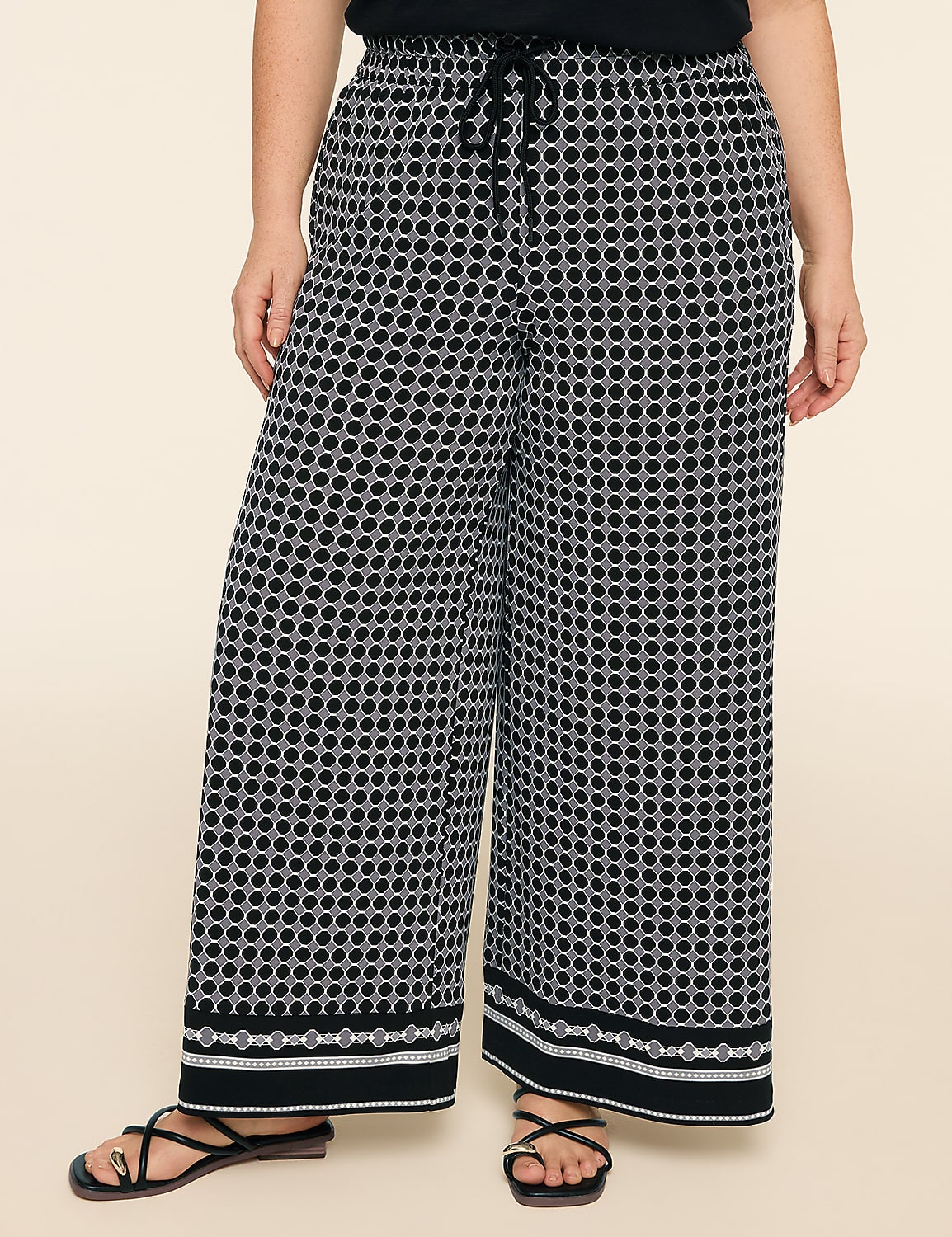 A person wearing black and white patterned wide-leg pants with a decorative hem stands against a plain beige background. Product Image 1