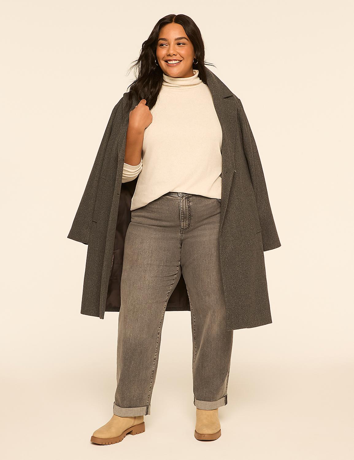 A smiling woman in a cream turtleneck, grey jeans, and tan boots stands in front of a plain beige background, with a grey coat draped over her shoulders. Product Image 3