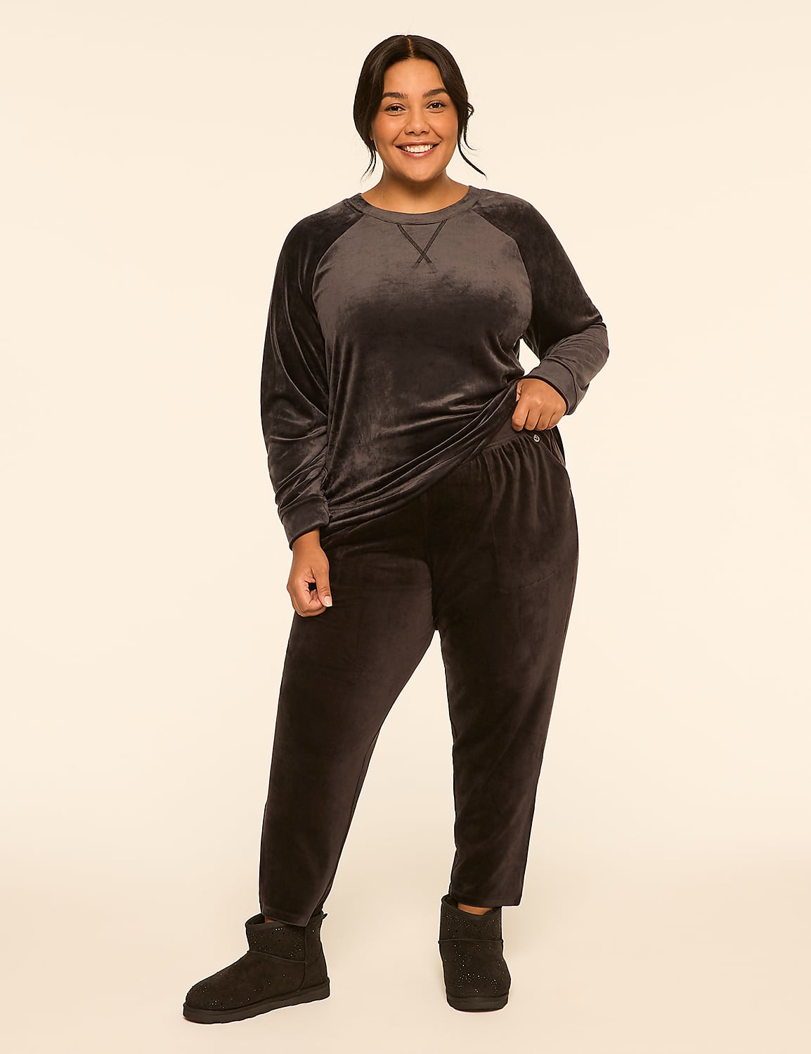 A smiling woman in a dark velvet loungewear set and Ugg boots stands against a plain, light beige background. Product Image 3