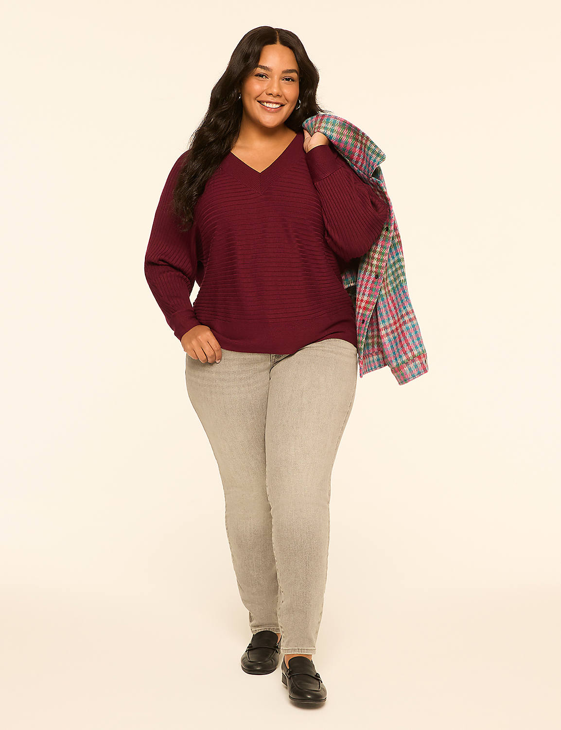 A smiling woman in a maroon sweater and grey pants stands against a plain, light-colored background with a plaid jacket draped over her shoulder. Product Image 3