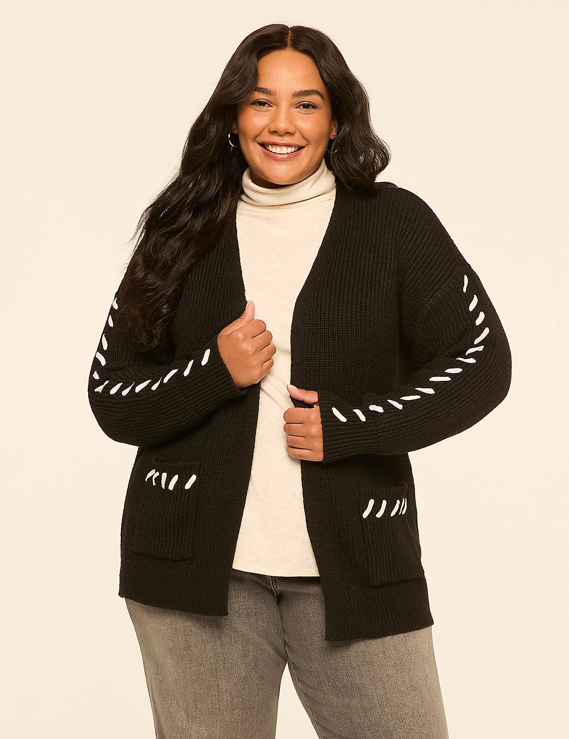 A smiling woman in a black cardigan with white stitching stands against a plain, light-colored background. Product Image 1