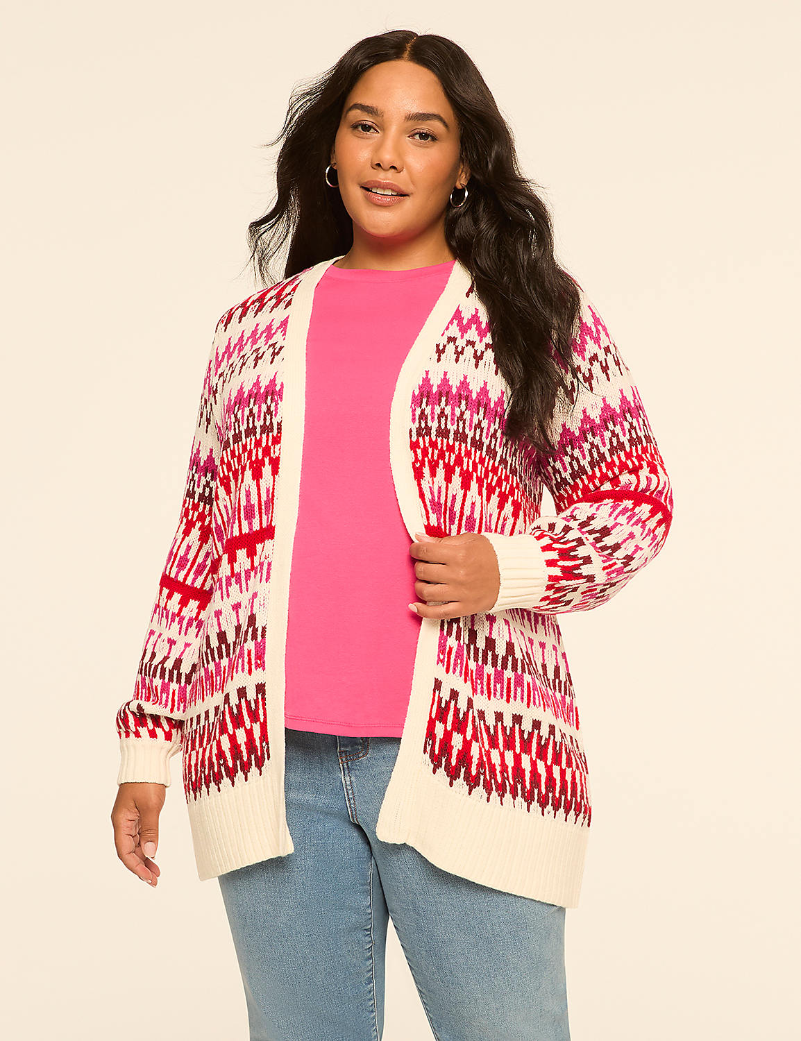 A woman in a pink shirt and blue jeans wears a cream-colored cardigan with a pink and red geometric pattern, standing against a plain beige background. Product Image 1