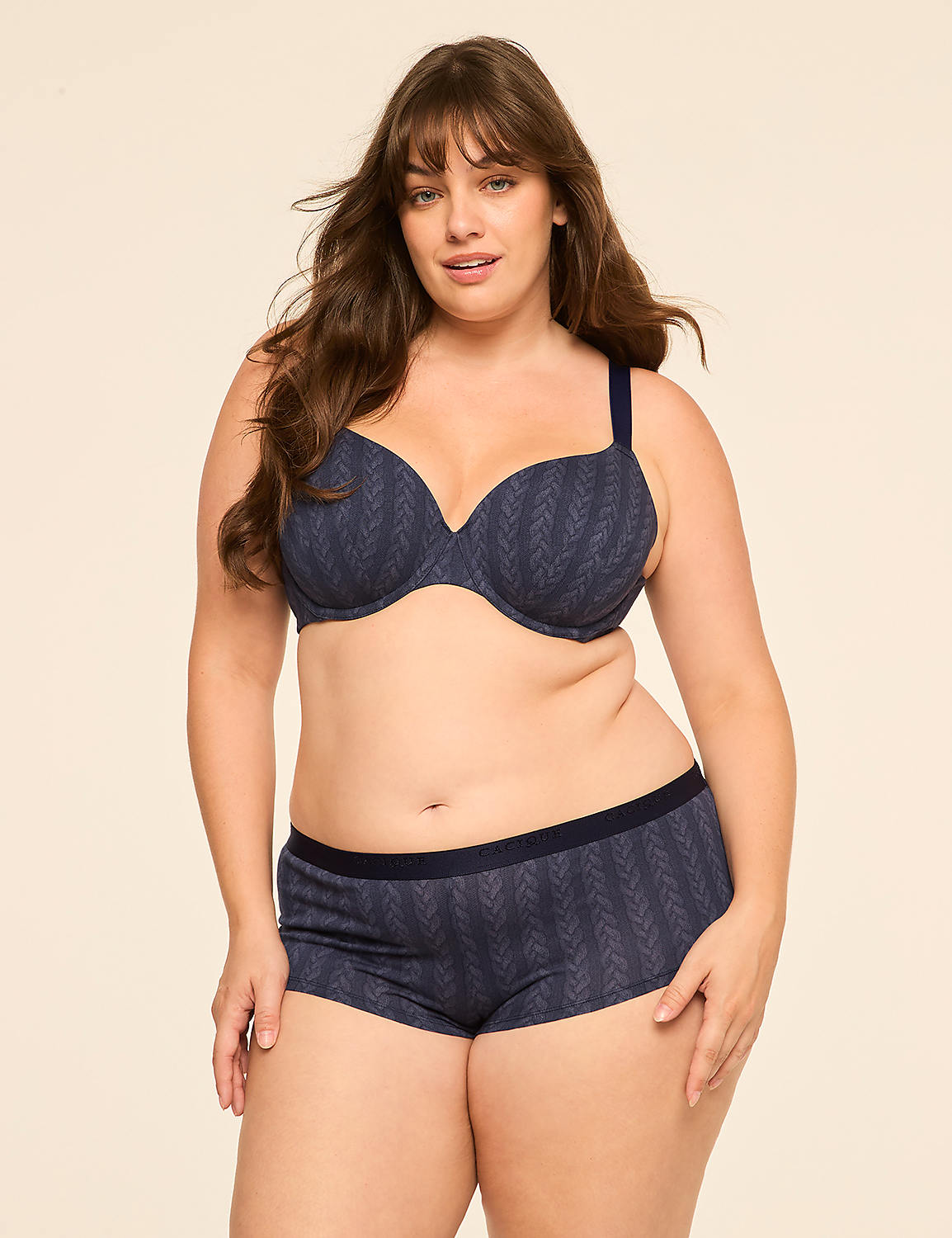 A woman with long brown hair stands in the foreground wearing a blue patterned bra and boy shorts against a plain, light-colored background. Product Image 4