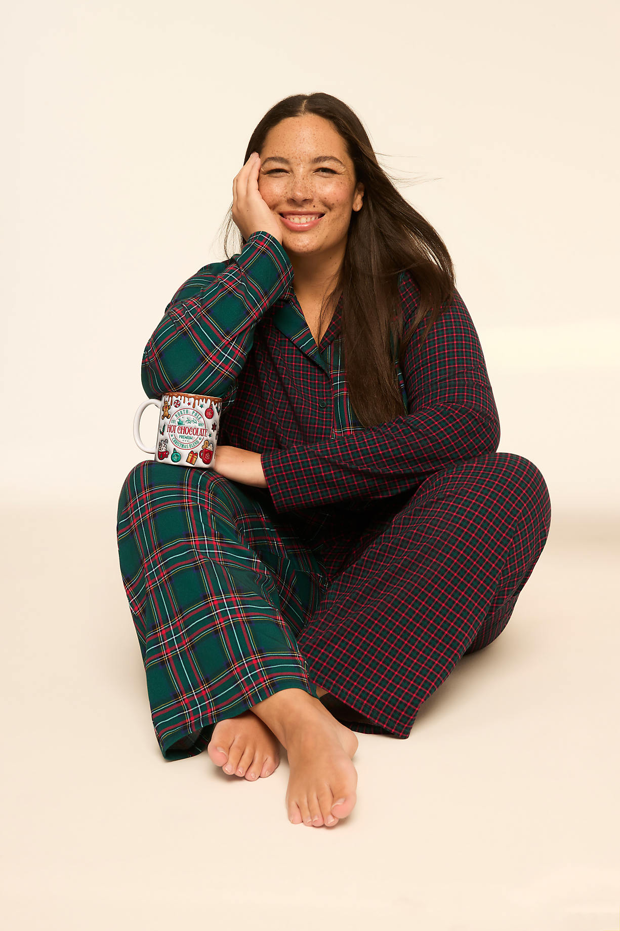 A woman in plaid pajamas sits on a plain background, holding a festive mug. Product Image 9