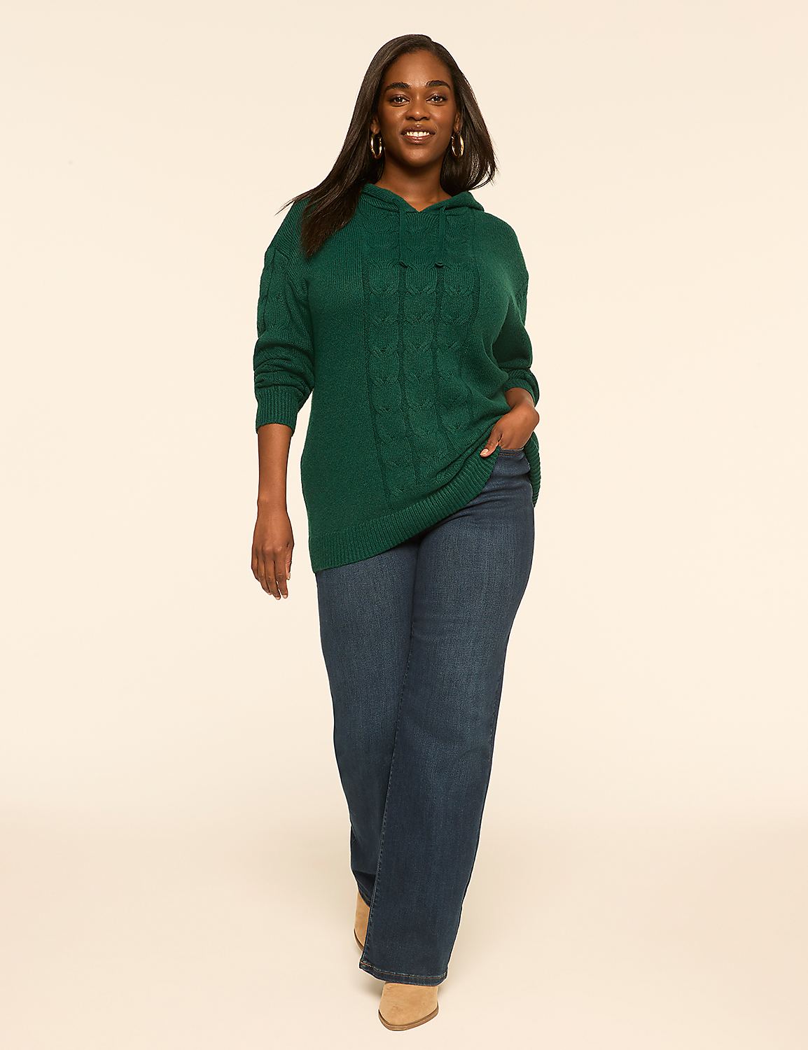 A smiling woman in a green cable-knit hoodie and dark wash jeans stands against a plain, light-colored background. Product Image 3