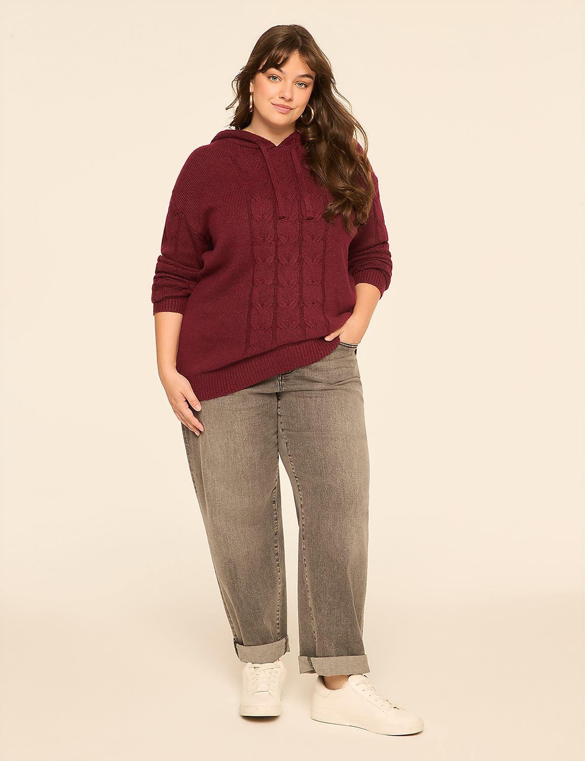 A woman in a burgundy cable-knit hoodie and gray jeans stands against a plain, light-colored background. Product Image 3