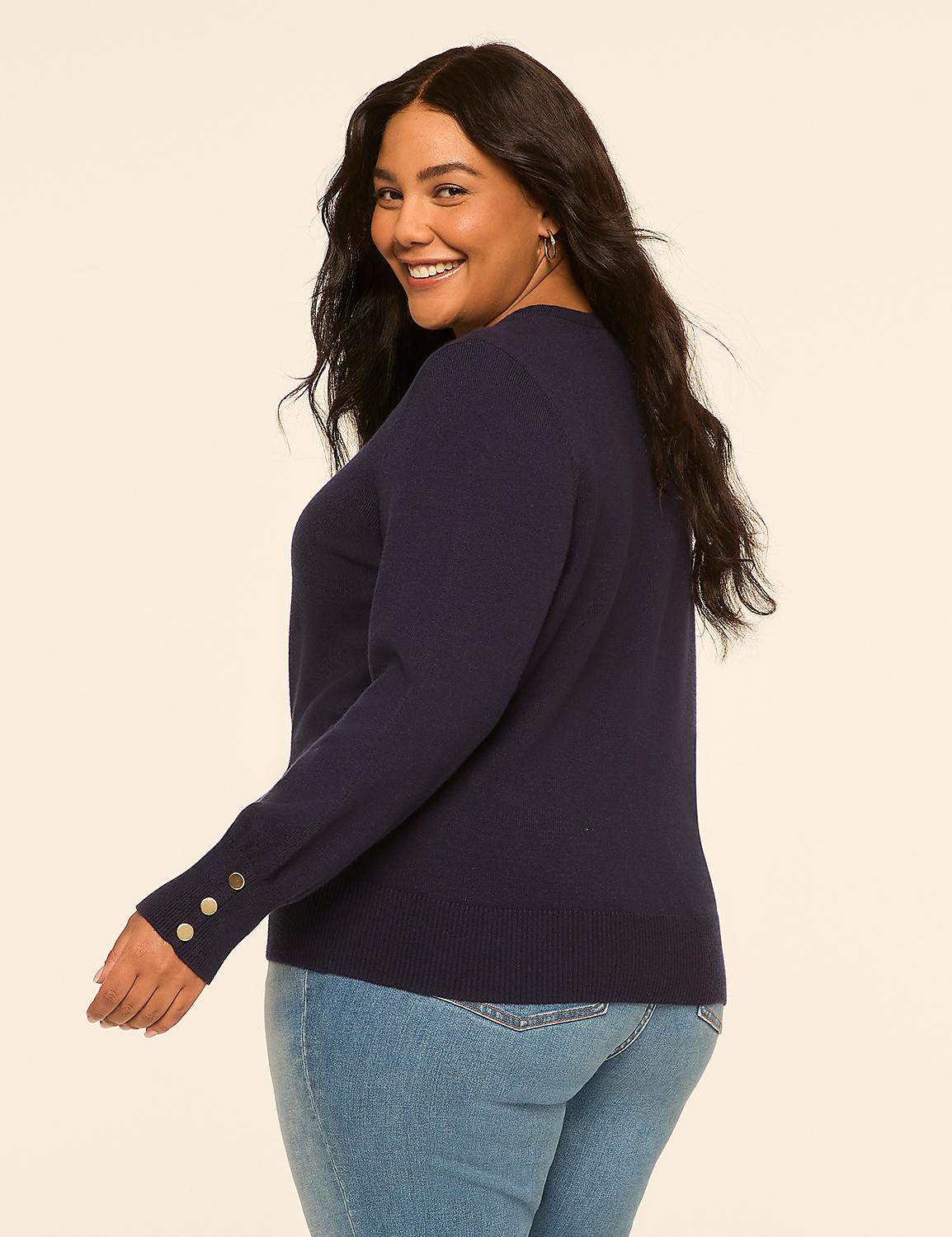 A woman in a navy sweater and jeans smiles over her shoulder against a plain, light-colored background. Product Image 2