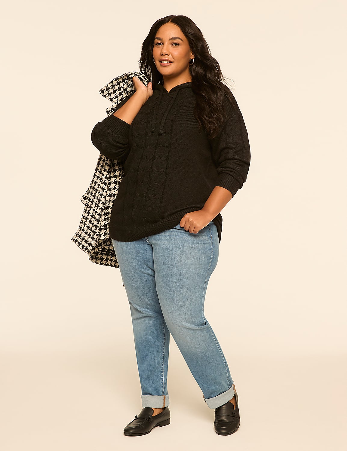 A woman in a black hoodie and jeans stands against a plain, light-colored background, with a patterned jacket draped over her shoulder. Product Image 3
