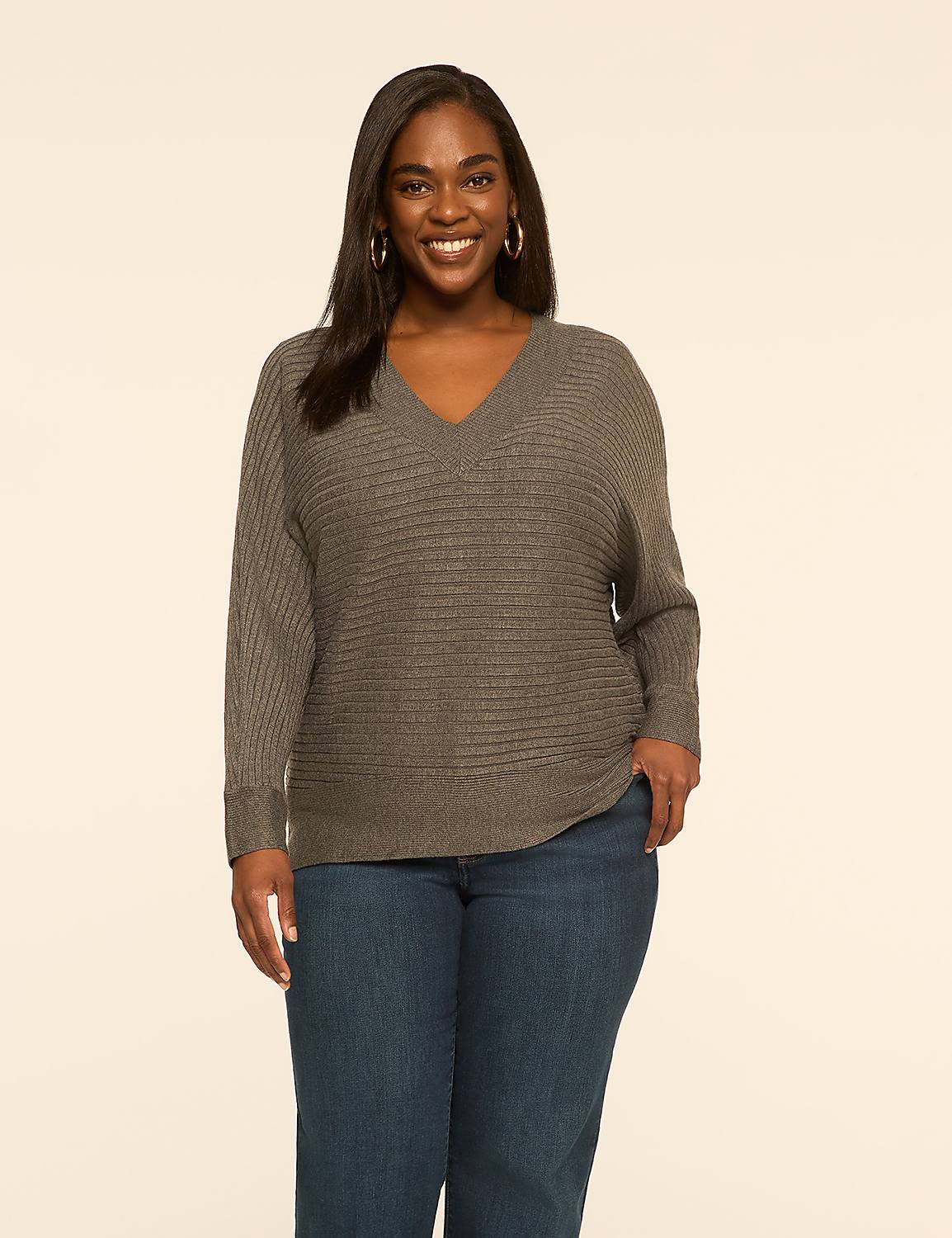 A smiling woman in a gray sweater and blue jeans stands against a plain, light-colored background. Product Image 1