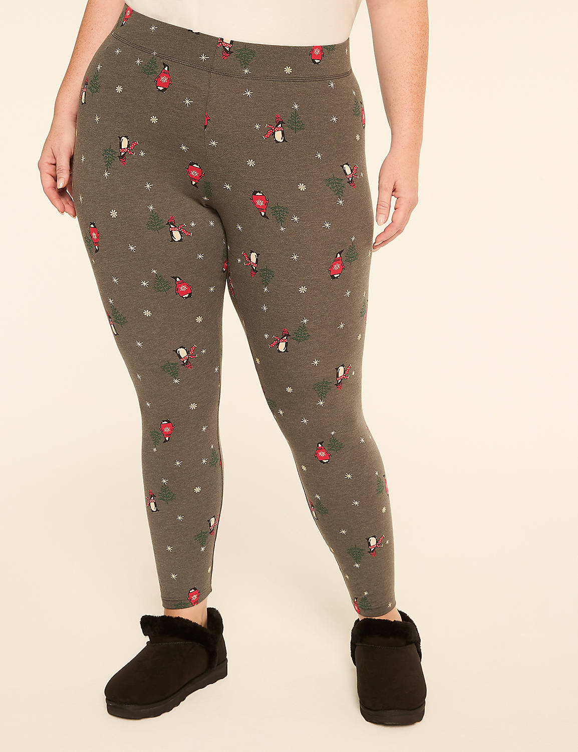 A person wearing grey leggings with a festive bird and snowflake pattern stands on a plain background, with black fuzzy slippers on their feet. Product Image 1