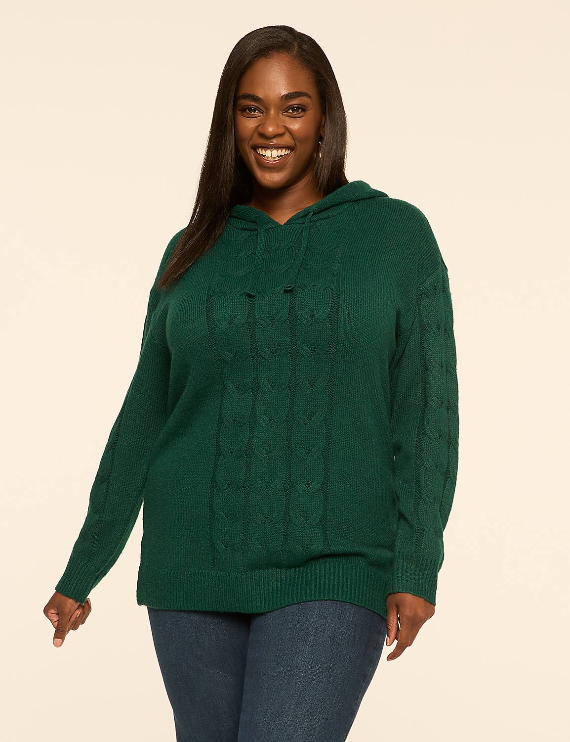 A smiling woman in a green cable-knit hoodie and blue jeans stands against a plain, light-colored background. Product Image 1