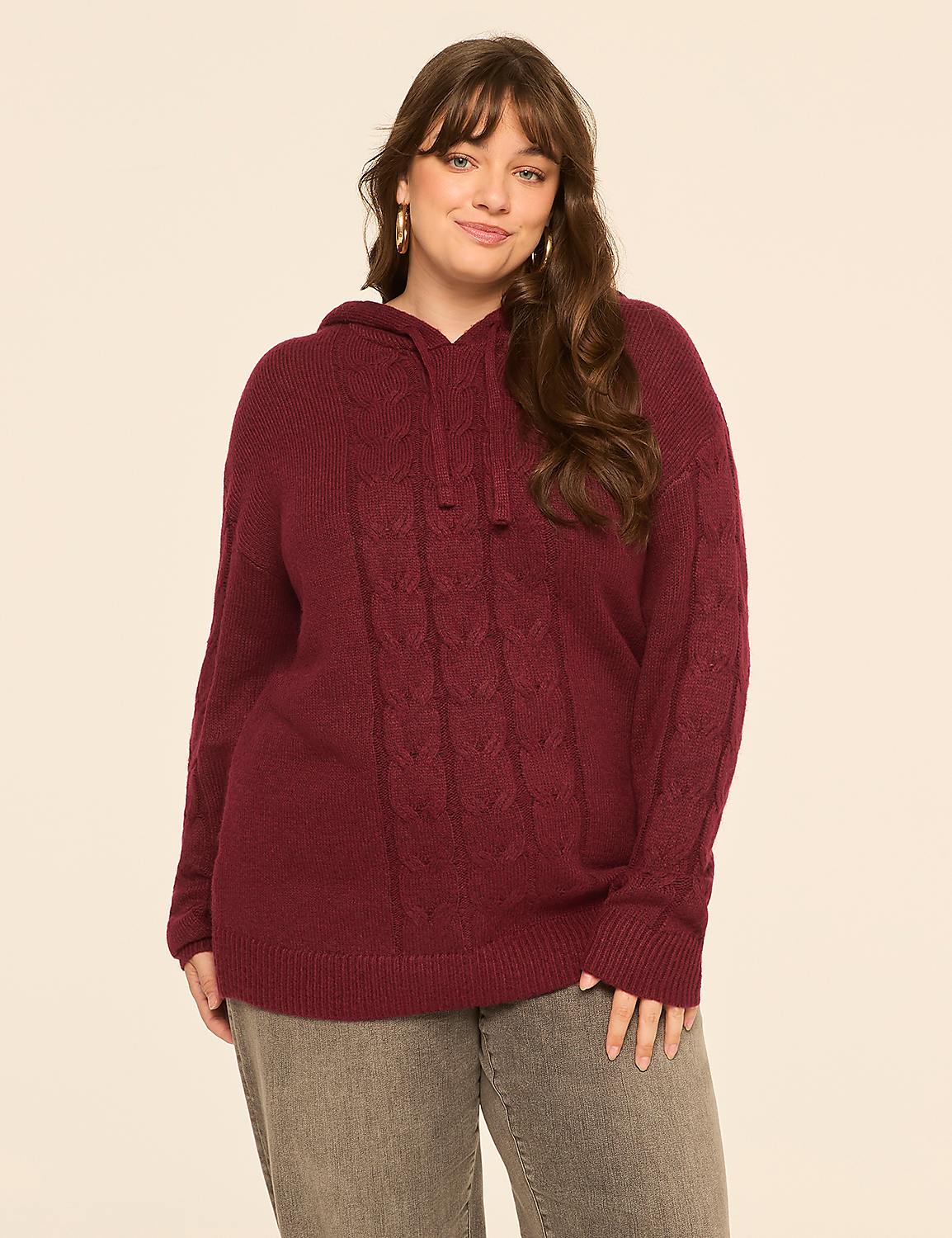 A woman in a burgundy cable-knit hoodie and gray jeans smiles against a plain, light-colored background. Product Image 1