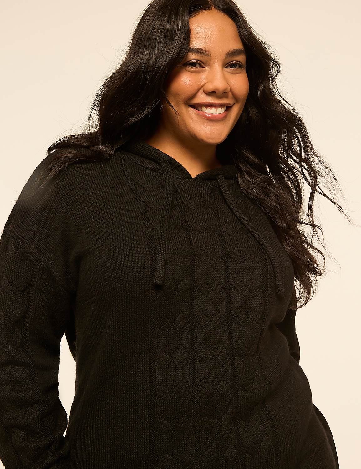 A smiling woman with long dark hair wears a black cable-knit hooded sweater against a plain, light-colored background. Product Image 4