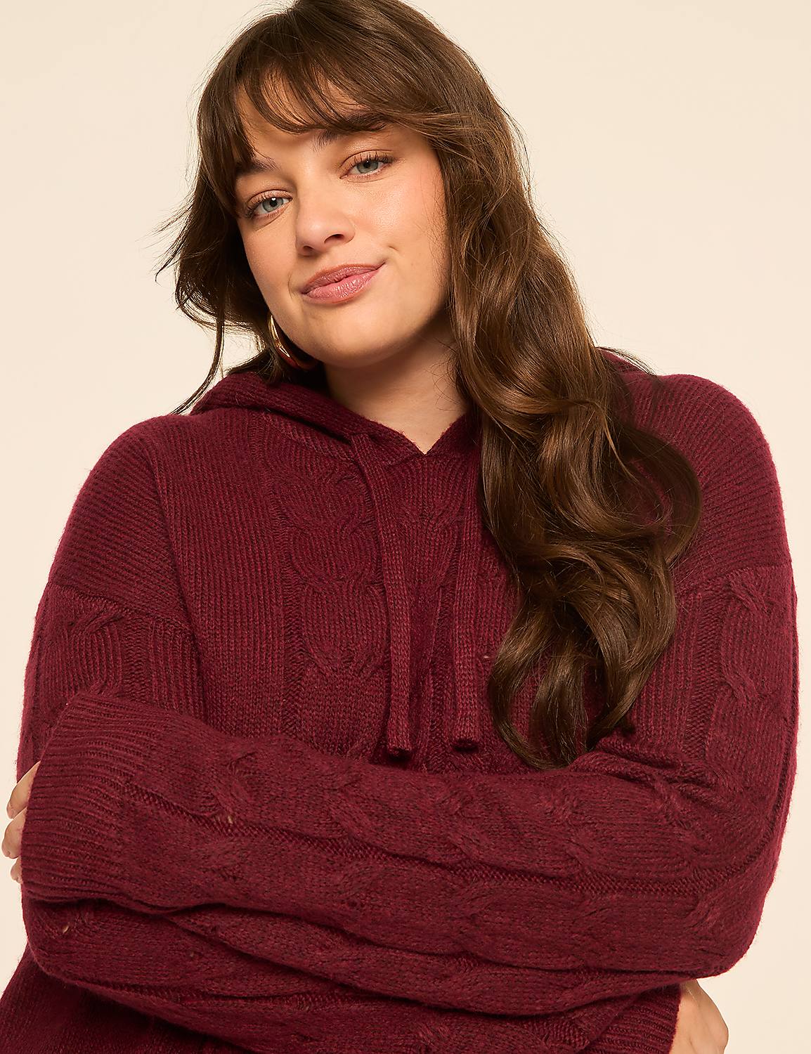 A young woman with long, wavy brown hair and bangs, wearing a burgundy cable-knit hooded sweater, smiles gently against a plain, light-colored background. Product Image 4