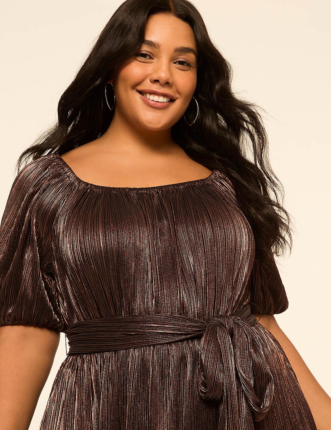 A smiling woman with dark, wavy hair wears a shimmering bronze dress with puffed sleeves and a belted waist, set against a plain, light-colored background. Product Image 3