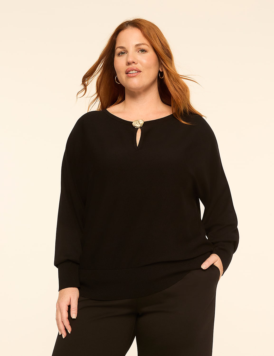 A woman with red hair and a black sweater stands against a plain, light-colored background. Product Image 1