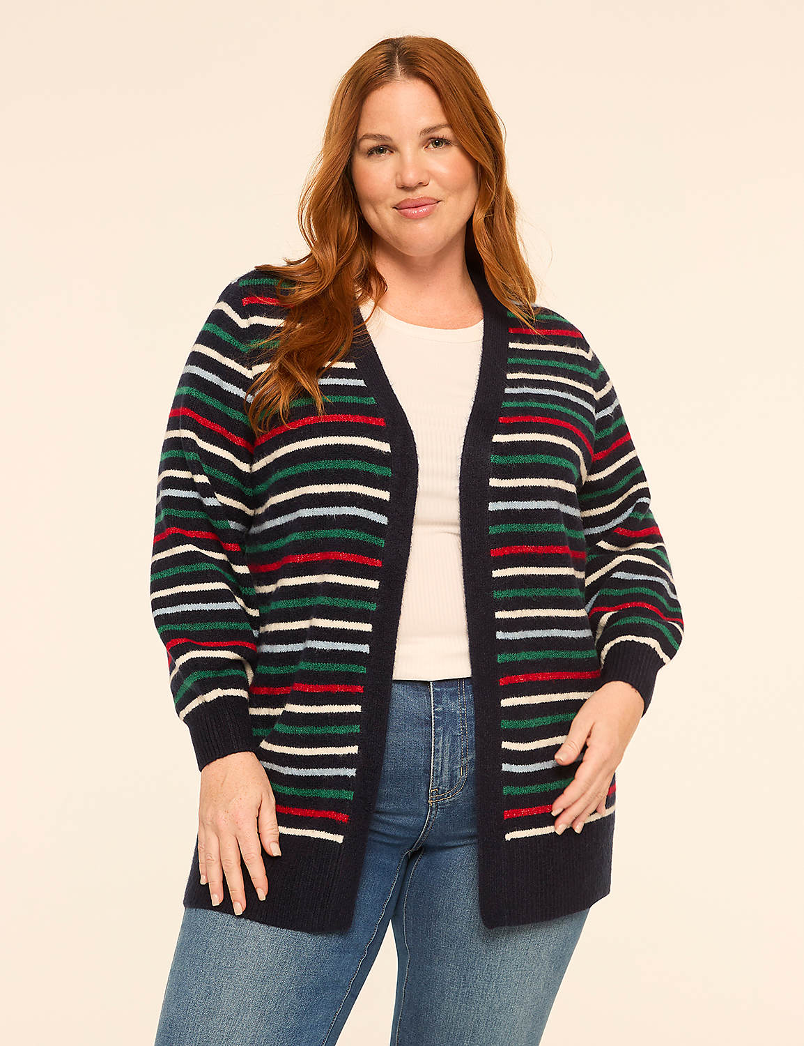 A woman with red hair stands in the foreground wearing a striped cardigan over a white top and blue jeans, against a plain, light-colored background. Product Image 1